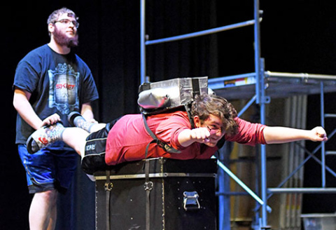 Patrick Star, played by Jacob Inman (center) blasts off with a jetpack for a scene in Aurora High School’s production of “The SpongeBob Musical” during a rehearsal on Friday. Giving Inman a boost during rehearsal is James Dieckmann.