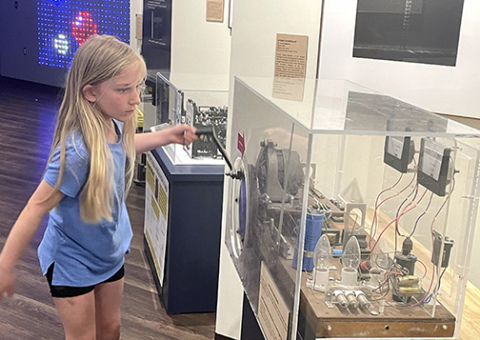 Greta Gustafson cranks with all her might to create an electrical charge that will cause the light bulbs to flash. Guests can test their strength at this exhibit in Edgerton’s reimagined Strobe Alley.