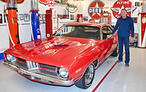 Mike Bish stands next to the red 1974 Plymouth Cuda in his Grand Island shop. He hopes it will soon by joined by the blue ‘71 Cuda he’s working on restoring. 