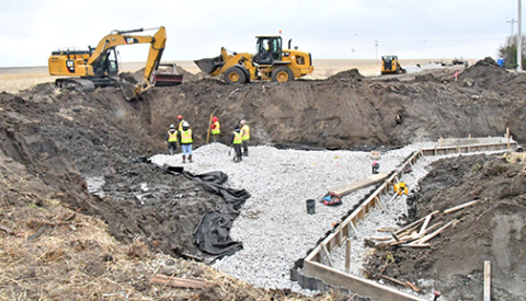 A construction crew excavates the bridge site and begins laying forms for pouring the floor of the box culvert that will replace the 1951 bridge on G Road. The footings of the culvert’s western headwalls can be seen at right.