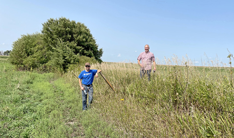 Two friends of David Meyer pose on Nebraska farm land to illustrate the impact of erosion and topsoil loss over many years. “These two fields were once the same level across the field fence; it is a striking difference,” Meyer said. The man on the right stands on unplowed prairie while the man on the right stands on land that has been in pasture for the last 20 years, but previous to that had been row cropped. 