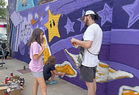 Josh Arias, who leads a nonprofit called Impact Art, works with Addi Aschenbrener, left, and Daylynn Egger, two of several youth who volunteered to help paint the lower portion of a mural at the Hamilton County Youth Center.