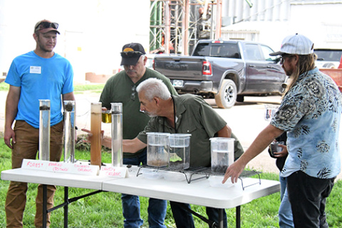 Ray Archuleta, center, conducts a demonstration Saturday at Grain Place Foods comparing how water moves through soil based on the amount of aggregates in the top few inches, which he said is improved if the ground is tilled less frequently and if cover crops are used.