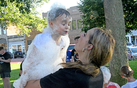 Kiersten Mersch blows some of the bubbles off the face of Creed Nisley after he spent time romping in the cloud of white stuff made by Edgerton’s bubble cannon on the west lawn of the courthouse. 