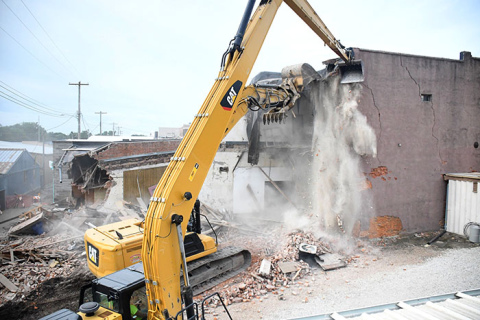 A cascade of dust falls from the roof and second floor of the former Gambles Store building in downtown Aurora as two huge excavators bring down the building a little at a time. 