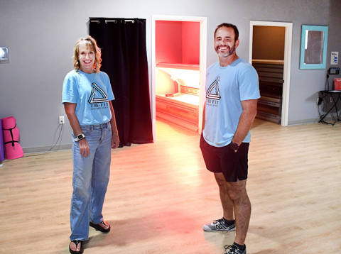 The glow of the Red Light Therapy room can be seen behind Tri-Fit owners Nick and Amy Owens.