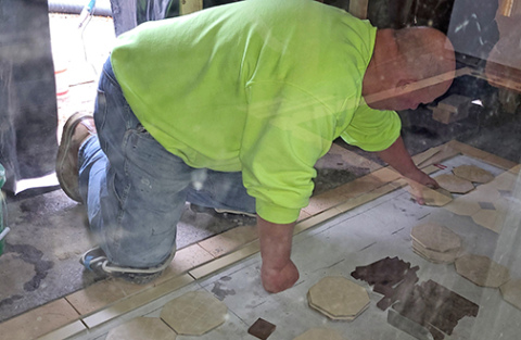 This photo, taken Monday morning from inside the courthouse through the glass front doors, shows a workman laying the tiles that will complete the outside landing of the building’s new east steps. The tiles match the original ones installed in the courthouse 130 years ago when it was built. 