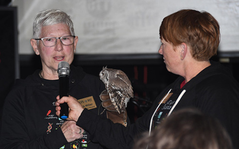 Deb Miller, left, holds one of the Edgerton’s winged friends as she explains a raptor experience being auctioned off. At right is Mary Molliconi.