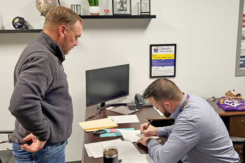 Hampton High School principal and soon to be superintendent, Carson Klute (right) signs the contract offered to him at Monday night's school board meeting. 