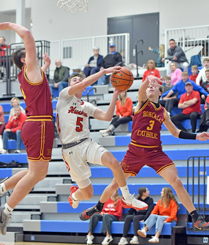 Aurora’s Ryan Staehr splits two Omaha Roncalli defenders on a dribble-drive second half play during a 54-41 loss to the Crimson Pride Monday. 