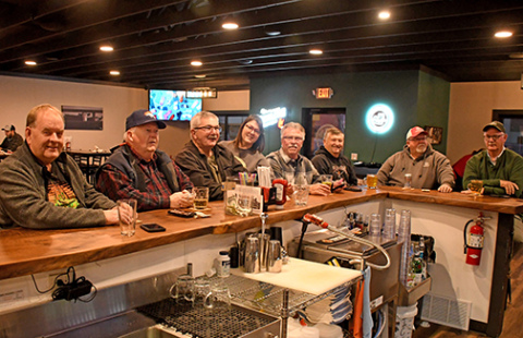 Members of the informal group calling itself “League” sit at the bar of the Loading Chute in Hampton on Monday night. One of the members joked that the group got its name because the men “compete” with the pickleball league that plays at the City Auditorium. With the group is Loading Chute bartender Annette Miller. Members in attendance Monday were, from left: John Kohtz, Tom Williamsen, Gene Winter, Tom Lindburg, Ed Dick, Robin Williamsen and Dean Klute. 