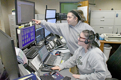 Headsets allow 911 dispatchers at the Hamilton County Dispatch Center to have their hands free while they are taking calls from the public. The tabletop microphone in front of dispatcher Jessie Boroff (seated) is used for contacting police officers and other personnel in the field. Also pictured is fellow dispatcher Melissa Barry. 