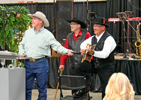 Harlan Schafer, right, plays a guitar he made especially for Friday’s Memorial Foundation auction. The item drew a winning bid of $2,200. Pictured with Schafer are auctioneers Mark and Kelly Kliewer.