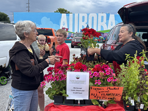 Nicole Alder, right, owner of Alder Plant Nursery, helps Betty Reddick with a purchase at Saturday morning’s Market on the Square event. This was the second week for the popular event, which is being held on the Heritage Bank south parking lot in front of the “Aurora” mural.