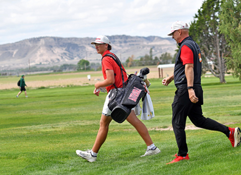 Cash Garrett walks off the No. 11 tee box at Scottsbluff Country Club with the Bluffs in the background and coach Craig Badura in tow. 