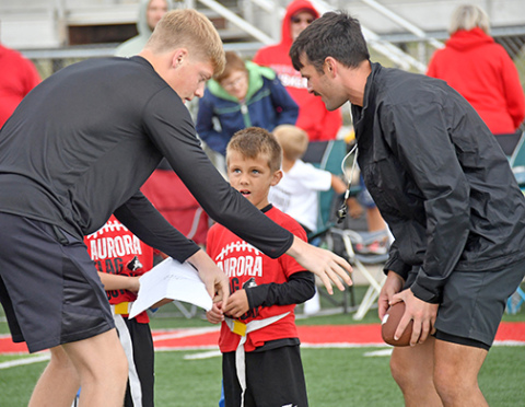 First grader Elijah Driewer receives some quarterback handoff advice from former Aurora QB1 Ethan Shaw (right) and his coach, Maddex Dummer.