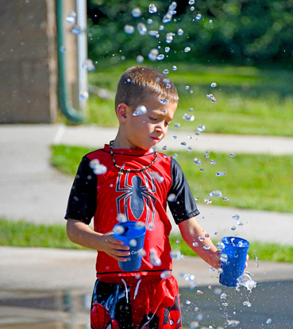 Luke Janzen fills up cups with water from the splash pad’s fountains during his family’s visit in the Thursday afternoon heat. The splash pad in Cole Park is now closed for the season.
