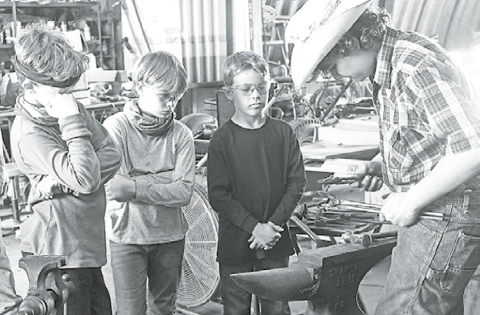 Thomas Ellis (left), Charlie Combe and fellow camper Zach Siem watch as Cooper Kremer demonstrates how they will be bending a piece of metal into a spiral. News-Register/Jeni Moellenberndt