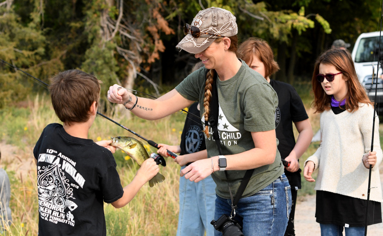 Heather Van Loh, whose military husband died several years ago, helps young members of A Soldier’s Child Foundation fish during a weekend outing at Timberlake Ranch Camp.