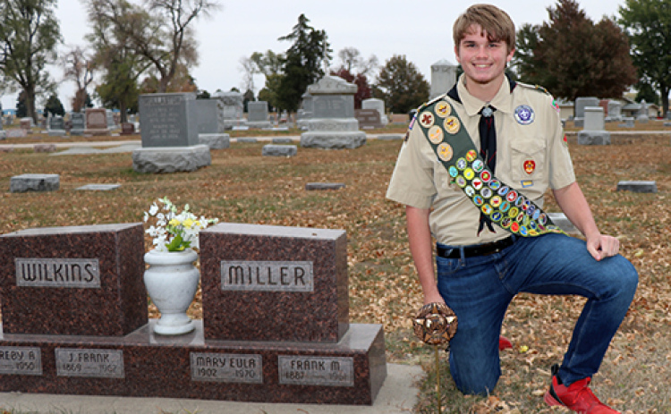 Astin Kennedy kneels next to one of the many markers that he placed in the Aurora Cemetery as part of his Eagle Scout project.