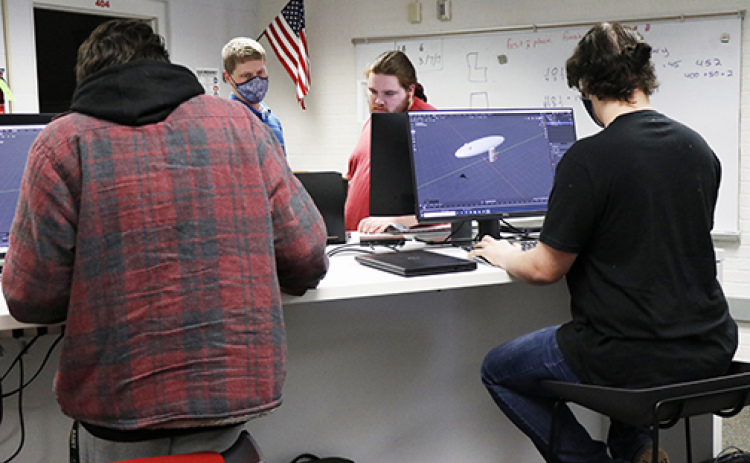 Jericho Stack (left), teacher Dustin Broeder, Logan Bennett and Brandon Krunovsky puzzle out a few pieces of their large project during Monday’s class.