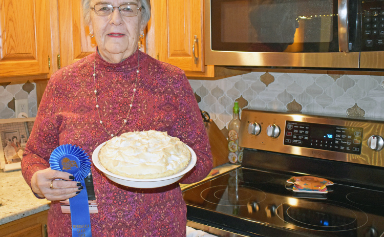 Berniece Luthy stands in her kitchen with her blue-ribbon worthy raisin sour cream pie. The blue ribbon pictured showcases just one of her Best of Division finishes at the Nebraska State Fair, where Luthy is also a volunteer.