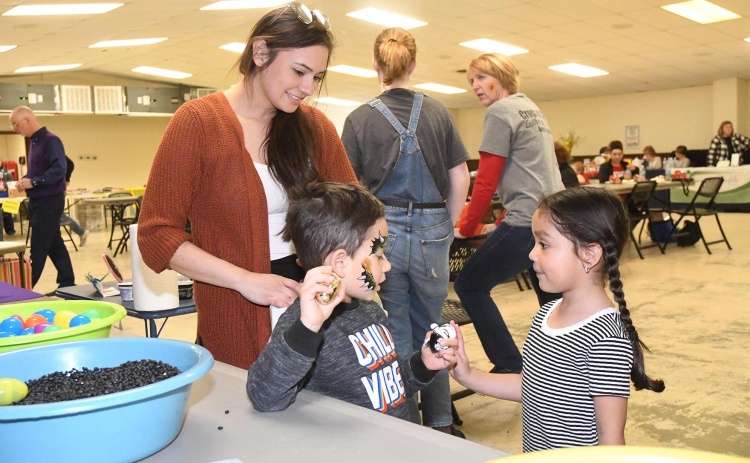 Melanie Dominguez (right) gives Attikus Louela a small plush tiger at the Early Childhood event  while his mother watches. Louela had just completed an egg shaker, which he holds in his left hand, when Dominguez gave him the toy.