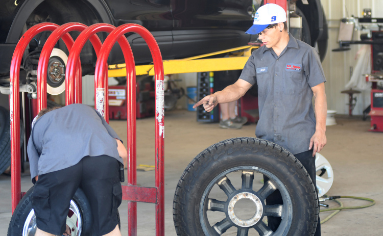 Mechanic Josh Moellenberndt (right) points out something to Blake Delarnn as they change out the tires on a state patrol vehicle in the background. Common parts like tires can now take days to arrove, while hard parts can take weeks up to a month.