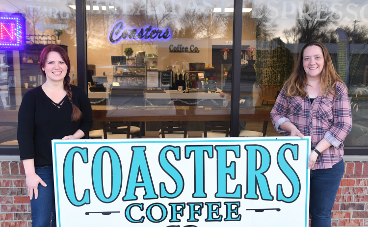 Sara Johnson (right) and Kandi Slocum hold up the sign to Coasters Coffee Co. outside the shop. Johnson stated she would transfer the business to employee and friend Kandi Slocum in early January.
