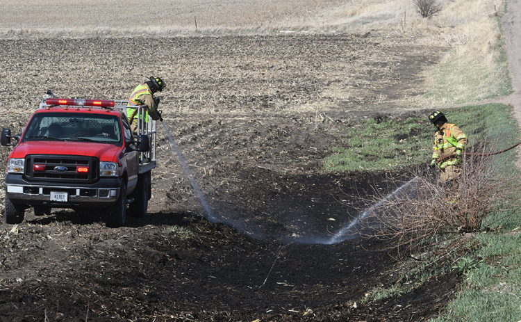 Two Aurora firefighters pour out water from hoses on burned ground after a ditch fire on S Road April 12. Fire Chief Tom Cox said the fire was started by lingering embers from before the burn ban and urged area residents to be vigilant even after fires are put out.