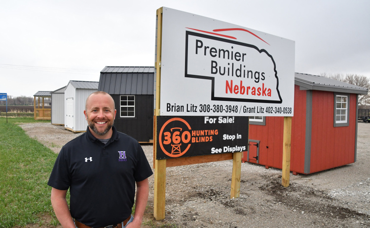Co-owner of Premier Buildings Nebraska Brian Litz stands near some buildings and his sign on North W Road near Hampton. He joined with his cousin Grant a year ago to sell buildings, trailers and deer blinds straight off his lot.