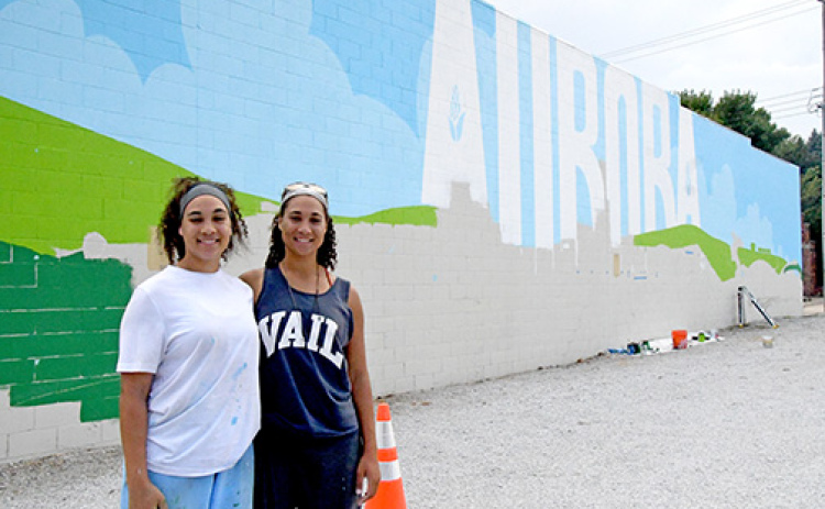 Artists Bristol, left, and Brianna Lewis stand next to the mural they are creating in downtown Aurora for the Hamilton Community Foundation.