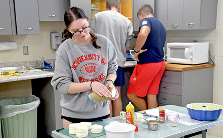Kylee Young makes monkey bread in Senior Seminar class on Thursday while Sam Wishman and Korbin Stump work on another part of breakfast in the background.