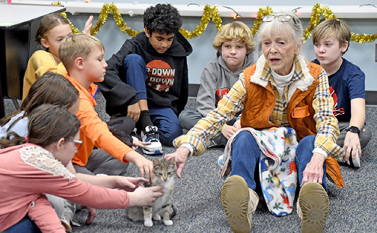 Aurora Adopt-A-Pet volunteer, Cathy Paule (right), talks to 5th graders about Adopt-A-Pet and how they can help the pets there as well as their own animals. At center is shelter kitten, Mimsey, who was brought to show the students as they celebrated the 20th season of  the Christmas Cheer class fundraiser.
