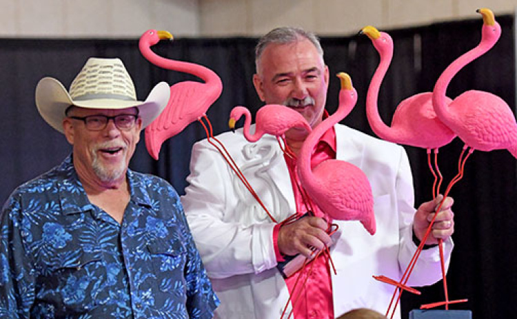 Jason Schneider, Memorial Foundation board chairman, holds some of the bright pink flamingoes sold during Friday’s Miami Vice Gala at the fairgrounds. At left is auctioneer Kelly Kliewer.
