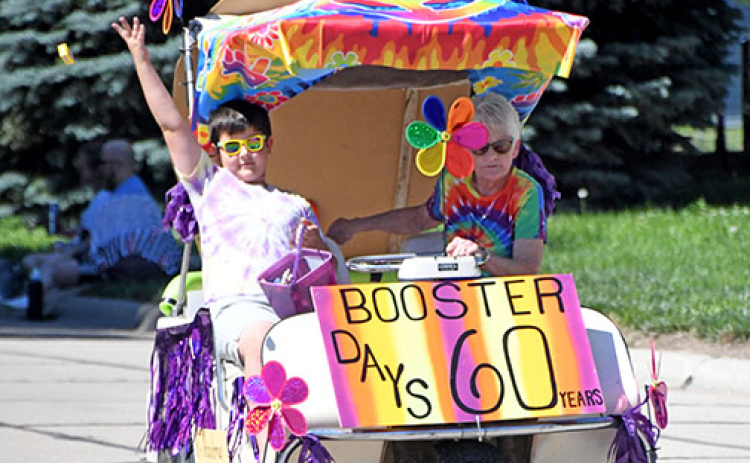 Damaris Olsen and her grandson, Reid, throw out candy to the crowd as they ride in the Booster Days Parade in their entry which won the award for Best Theme.