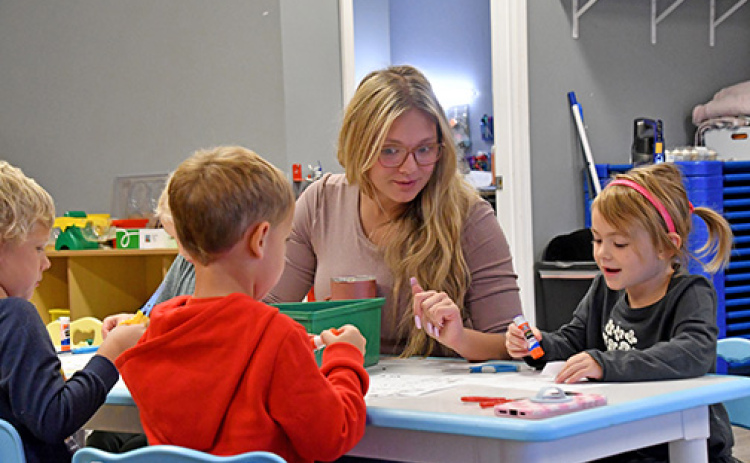 The Little Stingers Child Care Facility is set in motion to build a foundation on the empty lot south of Giltner Elementary School starting the third week of November. Staff member Gracie Oman (center) helps preschool students with their activity sheets during their morning class on Oct. 16. Students include, from left: Cyrus Wilcox, Thayer Barnes and Della Mae Lott.