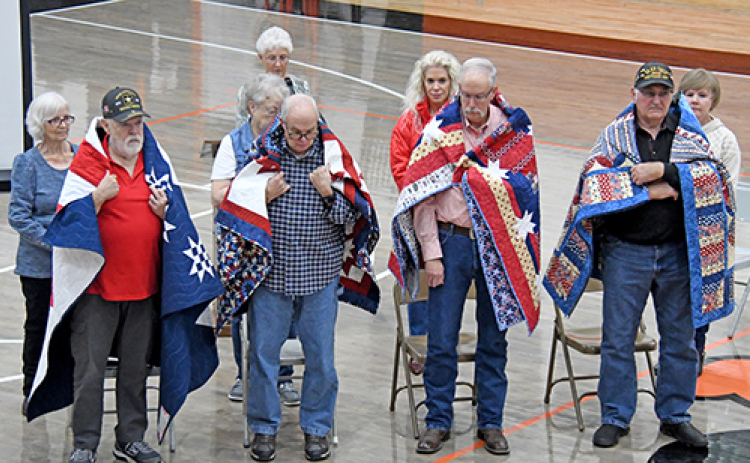 Four Giltner veterans were honored with Quilts of Valor during Giltner Public Schools’ Veterans Day program. The quilts were presented by the Nimble Thimble Quilt Guild, the Grand Island Quilt of Valor group. Veterans who received their quilt of valor includes, front from left: Allen Miller, Brian Miller, Kevin Miller, Kenneth Paul Colburn. The veterans were drapped with their quilts by Allen’s wife Kay, Janie Murphy, Darci Higgins Williamson and Kenneth’s wife Ann respectively during the ceremony.