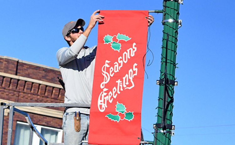 City crew member Riley Nuss hangs a Christmas banner on Aurora's downtown square