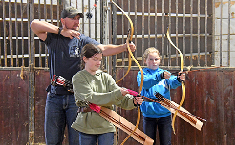 Great Plains Mounted Archery instructor Chris Patton shows his students, Londyn Ommert (left) and Penelope Mann how to adjust their bows for better aim.