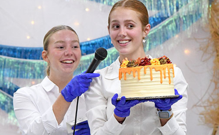 Makenna Oswald and Jasmine Hansen encourage guests to bid for one of the decorative cakes made for the Harvest Gala’s dessert auction Saturday night.