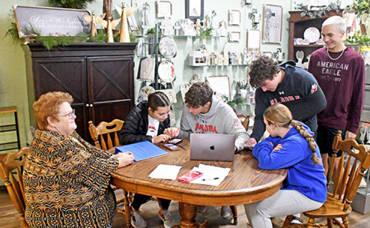 Angie Wall, left, owner of Honeysuckle Lane, watches as students from the Aurora High School marketing class work on a social media campaign to promote the store’s fall and Christmas sales and events. The students pictured are, from left, seated, Morgan Calkins, Parker Smith and Paityn Wyatt. Standing at right are Keegan Cheney and Jace Dorsey.