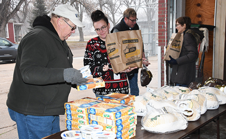 Food pantry volunteers help distribute bags packed with ham or turkey and all the trimmings for a special meal during Saturday’s annual holiday food distribution event.