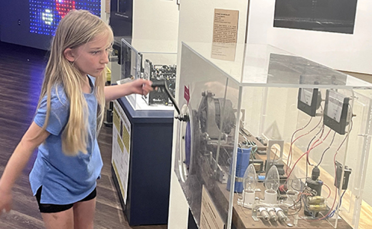 Greta Gustafson cranks with all her might to create an electrical charge that will cause the light bulbs to flash. Guests can test their strength at this exhibit in Edgerton’s reimagined Strobe Alley.