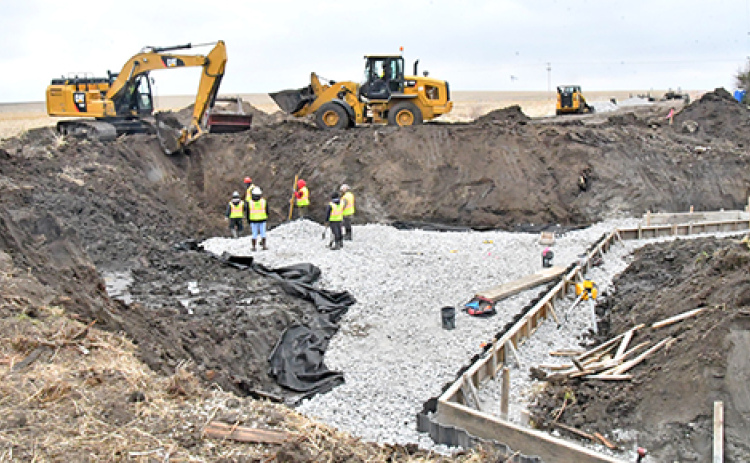 A construction crew excavates the bridge site and begins laying forms for pouring the floor of the box culvert that will replace the 1951 bridge on G Road. The footings of the culvert’s western headwalls can be seen at right.