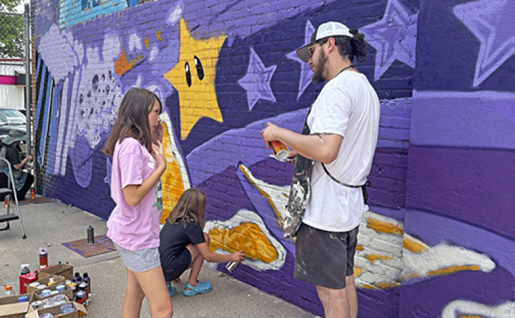 Josh Arias, who leads a nonprofit called Impact Art, works with Addi Aschenbrener, left, and Daylynn Egger, two of several youth who volunteered to help paint the lower portion of a mural at the Hamilton County Youth Center.