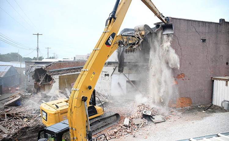 A cascade of dust falls from the roof and second floor of the former Gambles Store building in downtown Aurora as two huge excavators bring down the building a little at a time.