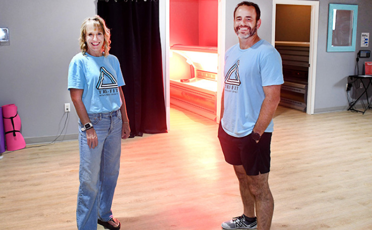The glow of the Red Light Therapy room can be seen behind Tri-Fit owners Nick and Amy Owens.