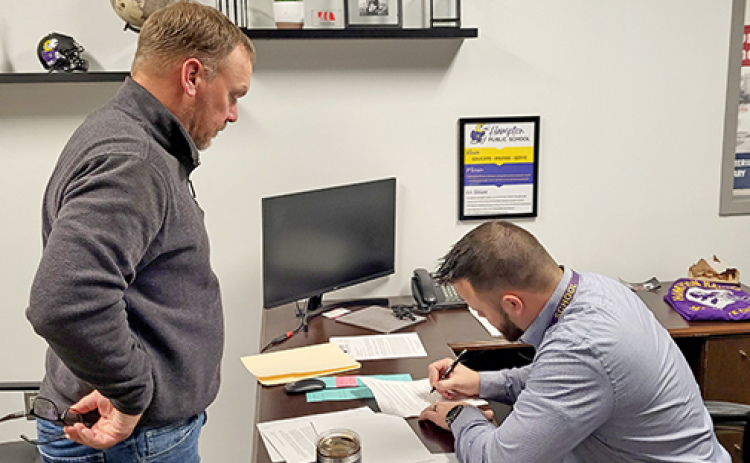 Hampton High School principal and soon to be superintendent, Carson Klute (right) signs the contract offered to him at Monday night's school board meeting.