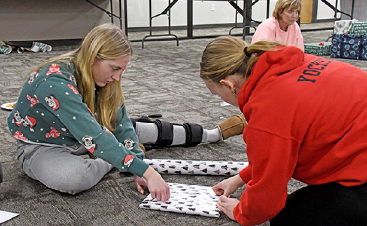 Aurora seniors Savanna James and Micole Yockey work on the finishing touches on one of the gifts that they wrapped Thursday during YEP’s gift-wrapping event.